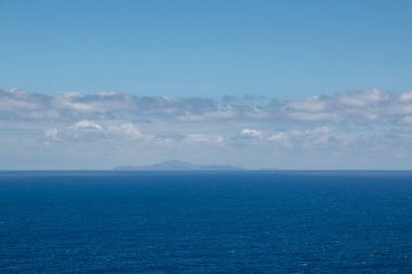 Atlantik okyanusunun sakin suları. Ufukta Madeira 'ya ait küçük adalar var. Beyaz bulutlu mavi gökyüzü. Görüntü: Vulcao Penha de Aquia, Madeira, Portekiz.