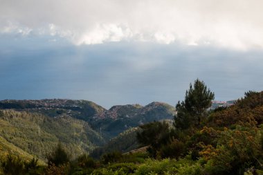 Dağlar taze yeşilliklerle kaplı. Bir bahar akşamı üzerlerinde bulutlar vardır. Risk Calheta, Miraduro do Rabacal, Madeira, Portekiz.