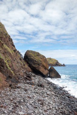 Adanın kuzeyindeki Atlantik Okyanusu kıyısındaki kayalıklar. Baharda beyaz bulutlu mavi gökyüzü. Ribeira da Janela, Madeira, Portekiz.