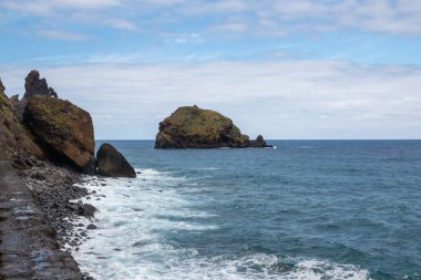 Adanın kuzeyindeki Atlantik Okyanusu kıyısındaki kayalıklar. Baharda beyaz bulutlu mavi gökyüzü. Ribeira da Janela, Madeira, Portekiz.