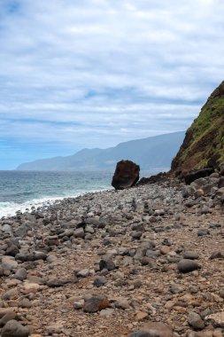 Volkanik kayalar adanın kuzeyinde Atlantik Okyanusu 'nun kıyısında yüksek uçurumlar oluşturur. Sakin turkuaz su ve beyaz bulutlu mavi gökyüzü. Ribeira da Janela, Madeira, Portekiz.