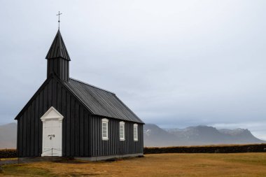 Kulede haçı olan siyah ahşap bir kilise. Beyaz detaylar. Okyanusa yakın bir yerde, bir yarımadada. Budakirkja, İzlanda.