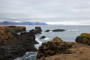 Cliffs on the coast of Atlantic ocean. Mountains on the horizon, partly covered with autumn clouds. Arnarstapi, peninsula Snaefellsnes, Iceland. clipart