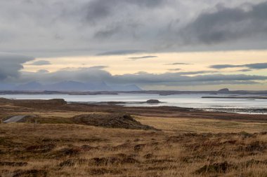 Kuzey Snaefellsnes 'den fiyordun dışındaki küçük adalara (Olafsey, Brokey, Oxney) bakın. Sahilde sonbahar otları, kayalar ve taşlar. Sonbaharda bulutlu bir gökyüzü. Batı İzlanda.
