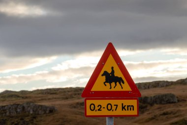 Trafik işareti, at binicileri uyarısı. Arka planda sarı çimenli ve bulutlu gökyüzü olan sonbahar manzarası. Hvanneyri, İzlanda.