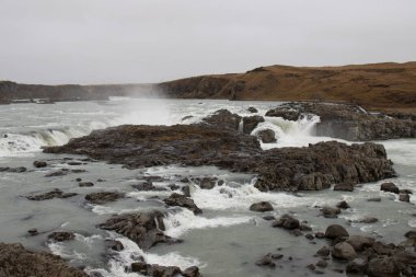 Waterfall in a valley on a river. Many volcanic rocks inside. Banks covered by autumn yellow grass. Urridafoss, Iceland. clipart