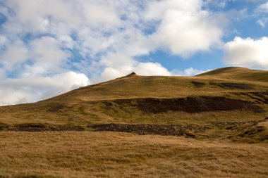Sonbaharda kadife bir yüzeye sahip olan volkanik kayalar ve dağlar, sarı yosun, liken ve çimenler sayesinde. Beyaz bulutlu mavi gökyüzü. Katla geopark, İzlanda.
