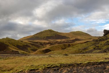 Sonbaharda kadife bir yüzeye sahip olan volkanik kayalar ve dağlar, sarı yosun, liken ve çimenler sayesinde. Beyaz bulutlu mavi gökyüzü. Katla geopark, İzlanda.