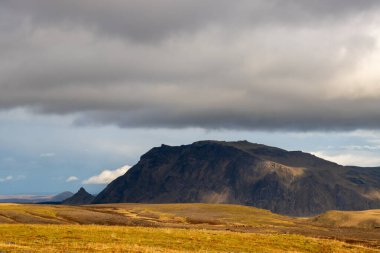 Sonbaharda kadife bir yüzeye sahip olan volkanik kayalar ve dağlar, sarı yosun, liken ve çimenler sayesinde. Beyaz bulutlu mavi gökyüzü. Katla geopark, İzlanda.