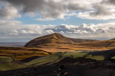 Volcanic rocks and mountains having a velvet surface in the autumn, thanks to the yellow moss, lichen and grass. Atlantic ocean in the background. Blue sky with white clouds. Katla geopark, Iceland. clipart