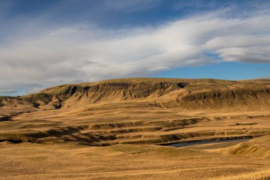 Dağlar yosun, ot ve liken ile kaplıdır. Sonbaharda güneşli güzel bir gün, altın otların rengini parlatıyor. Fjadra nehri bölgesi, Güney İzlanda, Kirkjubaejarklaustur yakınlarında..