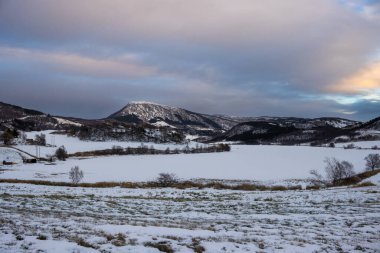 Kış manzarası ve karla kaplı bir ülke. Yüksek dağlar. Güneşin doğuşunda ve batışında bulutlu ve renkli bir gökyüzü. Harstad, Norveç.