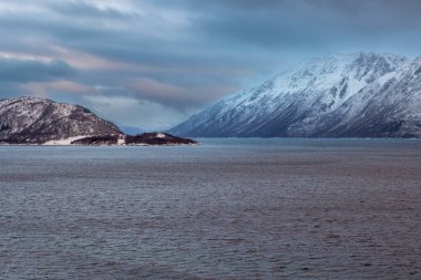 Karla kaplı bir manzara. Dağlar ve Kvaerfjord 'un suyu. Güneşin doğuşu / batışı sırasında bulutlu bir gökyüzü. Harstad, Norveç.