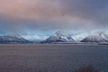 Karla kaplı bir manzara. Dağlar ve Kvaerfjord 'un suyu. Güneşin doğuşu / batışı sırasında bulutlu bir gökyüzü. Harstad, Norveç.