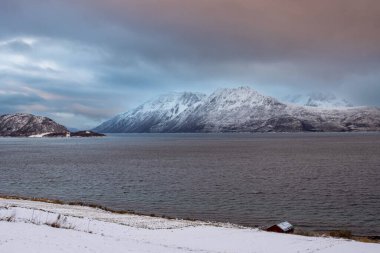 Karla kaplı bir manzara. Dağlar ve Kvaerfjord 'un suyu. Güneşin doğuşu / batışı sırasında bulutlu bir gökyüzü. Harstad, Norveç.