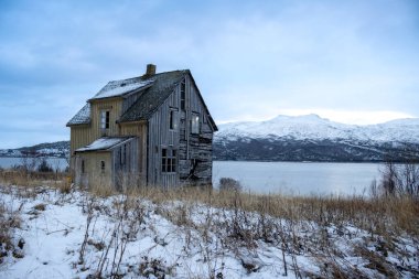 Norveç Denizi kıyısında terk edilmiş sarı ahşap bir ev. Arka planda dağlar. Sonbaharın sonlarında karla kaplı topraklar. Kongsvika, Norveç.