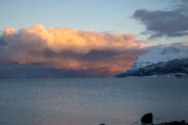 Calm water of the Norwegian sea. Reflection of the colorful sky at the sunrise of a short day in the late autumn. Mountains in the background. Cloudy sky. Tovik, Grovfjord, Norway. clipart