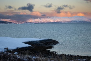Norveç denizinin sakin suları. Sonbaharın sonlarında kısa bir günün doğuşunda renkli gökyüzünün yansıması. Arka planda dağlar. Bulutlu gökyüzü. Tovik, Grovfjord, Norveç.