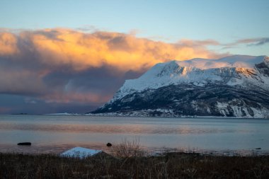 Norveç denizinin sakin suları. Sonbaharın sonlarında kısa bir günün doğuşunda renkli gökyüzünün yansıması. Arka planda dağlar. Bulutlu gökyüzü. Tovik, Grovfjord, Norveç.
