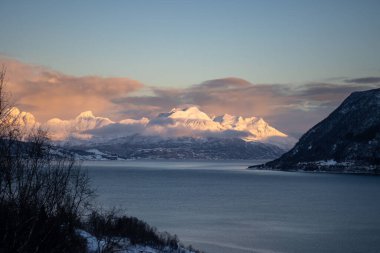 Dağlar Norveç Denizi 'nin sakin suyuyla kaplı. Kısa bir kutup gününün yüzeyinde ve günbatımında renkli bulutlar. Grovfjord, Norveç.