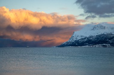 Calm water of the Norwegian sea. Reflection of the colorful sky at the sunrise of a short day in the late autumn. Mountains in the background. Cloudy sky. Tovik, Grovfjord, Norway. clipart