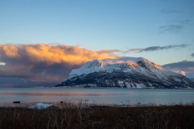 Norveç denizinin sakin suları. Sonbaharın sonlarında kısa bir günün doğuşunda renkli gökyüzünün yansıması. Arka planda dağlar. Bulutlu gökyüzü. Tovik, Grovfjord, Norveç.