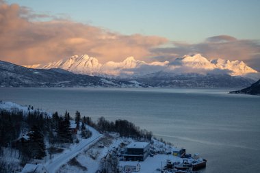 Dağlar Norveç Denizi 'nin sakin suyuyla kaplı. Kısa bir kutup gününün yüzeyinde ve günbatımında renkli bulutlar. Grovfjord, Norveç.