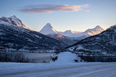 Dağlar Norveç Denizi 'nin sakin suyuyla kaplı. Kısa bir kutup gününün yüzeyinde ve günbatımında renkli bulutlar. Grovfjord, Norveç.