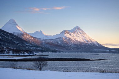 Dağlar Norveç Denizi 'nin sakin suyuyla kaplı. Kısa bir kutup gününün yüzeyinde ve günbatımında renkli bulutlar. Grovfjord, Norveç.