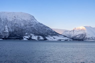 Dağlar Norveç Denizi 'nin sakin suyuyla kaplı. Kısa bir kutup gününün yüzeyinde ve günbatımında renkli bulutlar. Grovfjord, Norveç.