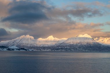 Dağlar Norveç Denizi 'nin sakin suyuyla kaplı. Kısa bir kutup gününün yüzeyinde ve günbatımında renkli bulutlar. Grovfjord, Norveç.