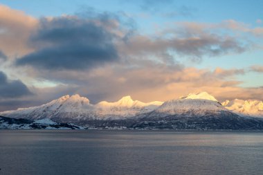 Dağlar Norveç Denizi 'nin sakin suyuyla kaplı. Kısa bir kutup gününün yüzeyinde ve günbatımında renkli bulutlar. Grovfjord, Norveç.