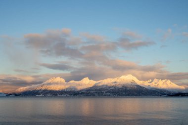 Dağlar Norveç Denizi 'nin sakin suyuyla kaplı. Kısa bir kutup gününün yüzeyinde ve günbatımında renkli bulutlar. Grovfjord, Norveç.