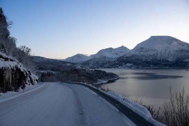 Karla kaplı bir ülke. Fiyortta sakin su (Norveç denizi). Karlı dağlar. Gökyüzü açık. Tennevoll, Norveç.