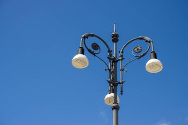 Gündüz vakti güneş ışığıyla aydınlanan üç modern ampulle süslenmiş bir sokak lambası. Arka planda açık mavi gökyüzü. Avola, Sicilya, İtalya.