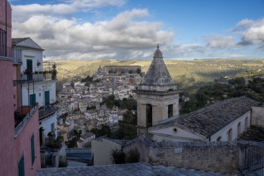 Tepedeki eski bir şehrin barok tarihi mimarisinin ayrıntıları. Bir kilise kulesi ve etraftaki evler. Baharda beyaz bulutlu mavi gökyüzü. Ragusa, Sicilya, İtalya.