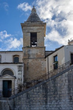 Tepedeki eski bir şehrin barok tarihi mimarisinin ayrıntıları. Bir kilise kulesi ve etraftaki evler. Baharda beyaz bulutlu mavi gökyüzü. Ragusa, Sicilya, İtalya.