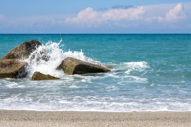 Calm turquoise water of the Tyrrhenian (Mediteranean) sea. Artificial and natural breakwaters. Horizon of the water and sandy beach. Blue sky with white clouds in the spring. Spadafora, Sicily, Italy. clipart