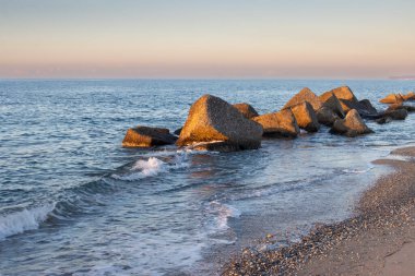 Sandy beach with rocks on the coastline sunlight of an sunset. Calm water of Tyrrhenian (Mediterranean) sea. Colorful sky with light clouds. Spadafora, Sicily, Italy. clipart