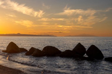 Sandy beach with rocks on the coastline sunlight of an sunset. Calm water of Tyrrhenian (Mediterranean) sea. Colorful sky with light clouds. Spadafora, Sicily, Italy. clipart