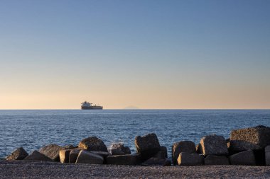 Tyrhenian (Akdeniz) denizinin sakin koyu mavi suları. Sahilde dalgalar. Ufuktaki büyük gemi ve Aeolian adaları. Gün batımının erken saatlerinde mavi gökyüzü ve turuncu ışık. Caldera, Sicilya, İtalya.