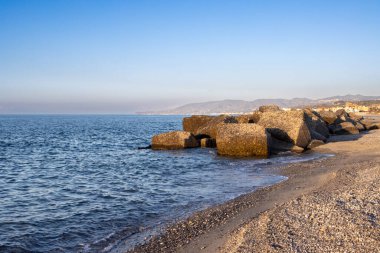 Dalgalı sahil. Tyrhenian (Akdeniz) denizinin sakin mavi suları. Gün batımında turuncu tonları olan mavi gökyüzü. Spadafora, Sicilya, İtalya.