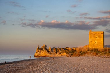 Tyrhenian kumsalı (Akdeniz) denizi. Kıyıdaki kayalıklardaki eski tarihi bina. Mavi akşam gökyüzü. Altın saatinde güneş ışığı. Kampofelice di Roccella, Sicilya, İtalya.