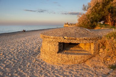 Sandy beach of the Tyrrhenian sea. Bunker from the World War 2 illuminated by the light of sunset. Greenery in the background. Blue sky with small clouds. Campofelice di Roccella, Sicily, Italy. clipart