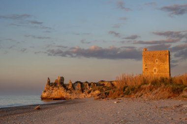 Tyrhenian kumsalı (Akdeniz) denizi. Kıyıdaki kayalıklardaki eski tarihi bina. Mavi akşam gökyüzü. Altın saatinde güneş ışığı. Kampofelice di Roccella, Sicilya, İtalya.