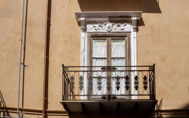 Balkon kapısının dekoratif çerçevesi. Yenilenmiş eski bir turuncu evin cephesi. Parlak güneş ışığı. Cefalu, Sicilya, İtalya.