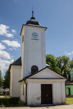 Siyah detayları ve çatısı olan beyaz şapel. Saati olan kule. Kilisenin yanından geç. Beyaz bulutlu mavi gökyüzü. Lestina, Moravya (Morava), Çek Cumhuriyeti.