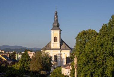 Siyah çatılı Aziz Bartholomew Kilisesi 'nin beyaz-sarı cephesi. Çapraz kule. Mavi gökyüzü. Arka planda dağlar. Zabreh, Moravya (Morava), Çek Cumhuriyeti.