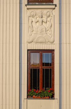 Simple traditional wooden brown window with a reflection. Flower pot full of red pelargonium. Ornate pastel yellow facade of the house with art deco element. Mohelnice,Moravia (Morava), Czech republic clipart