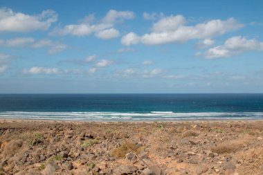 Atlantik Okyanusu kıyısındaki volkanik kayalar. Beyaz kumlu bir sahil. Kışın bulutlu bir gökyüzü. Famara, Lanzarote, Kanarya Adaları, İspanya.